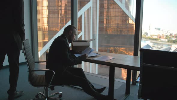 A Young Men Unpacks a Cardboard Box with Documents and Self Items in a New Office alt