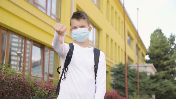 A Caucasian Teenage Boy in a Face Mask Shows a Thumb Down to the Camera and Shakes His Head