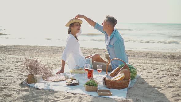 Happy Young Beautiful Couple Celebrating Love and Valentines Day Sitting on Sand Beach at Sea Coast alt