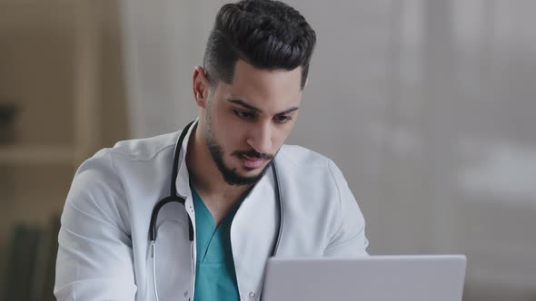 Concentrated Man Hispanic Doctor Physician Wear White Coat Use Computer Internet at Desk Type Recipe alt