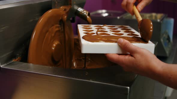 Worker filling mould with melted chocolate alt