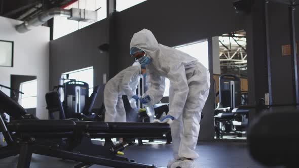 Team of health workers wearing protective clothes cleaning gym by using disinfectant sprayer alt