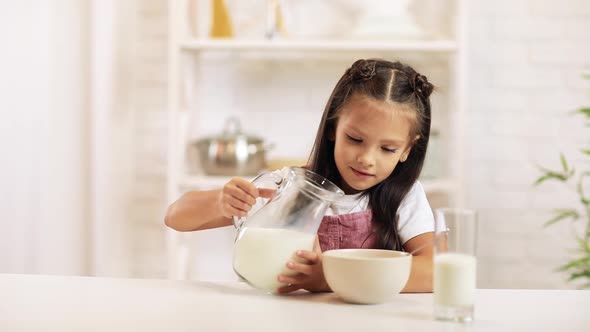 Child Pours Milk Into a Bowl of Cereal in the Kitchen.