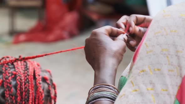 African Woman Weaving African Braids with Red Kanekalon Outdoor Zanzibar Africa alt