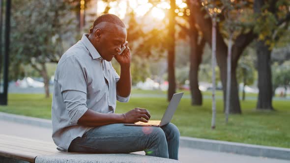 African American Man Experienced Professional Talking on Phone Using Laptop Computer Sitting alt