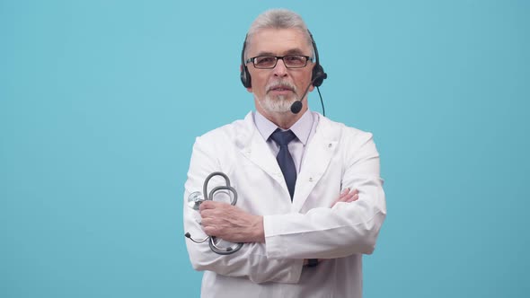 Man a Medical Gown Stands in a Headset and Talks Holding with Hand Stethoscope in the Studio alt