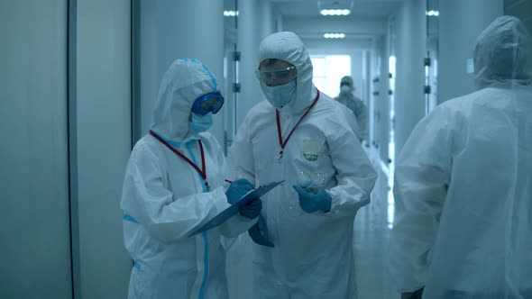 Hospital Workers in Hazmat Talk in a Hallway. alt