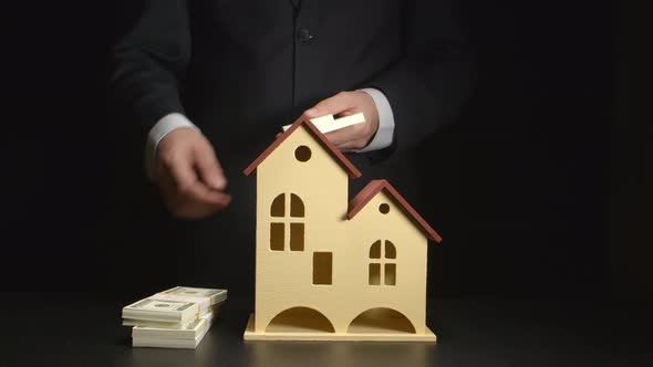 Businessman counts a money and throws it on a table near a house model