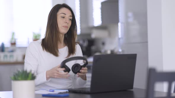 Woman putting on headphones for video call on laptop
