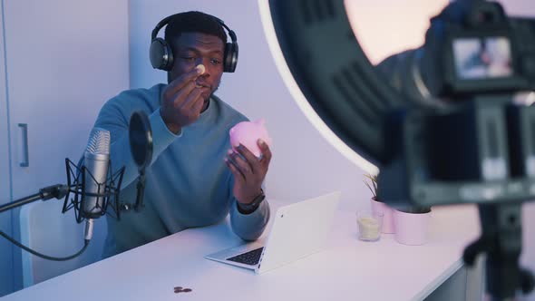 Man Wearing Headphones and Holding a Piggy Bank Recording a Video alt