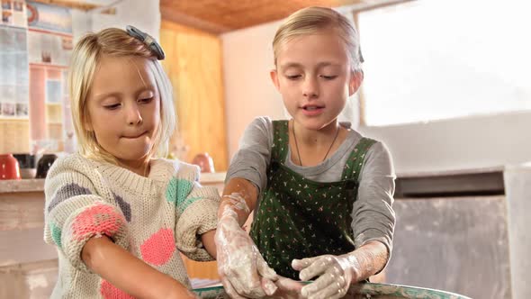 Girl assisting her sister while making a pot alt