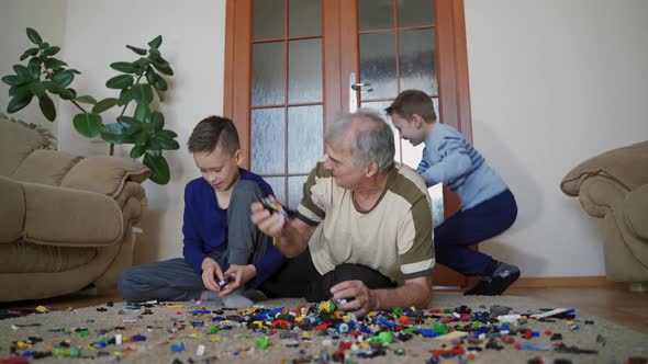 Old man with little boys playing with lots of colorful plastic toys indoor alt