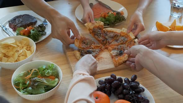 Many hands taking slices of pizza on the dining table.