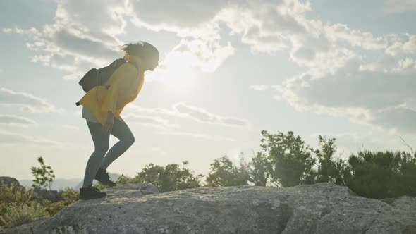 The Girl Climbs the Rocks to the Top of the Mountain and Raises Her Hands Uphill alt