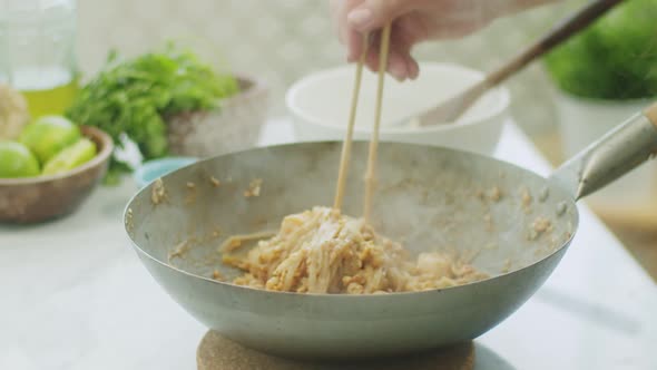 Woman stirring hot wok noodles with chopsticks alt
