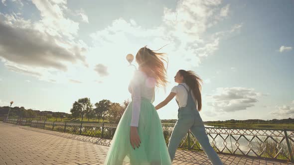 Two Friendly Girlfriends Run in a Jump Holding Hands at Sunset alt