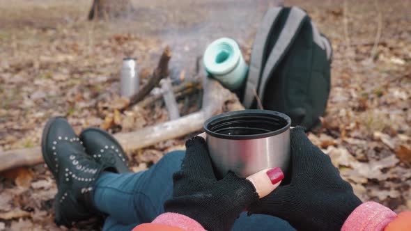 Girl Having Rest with Hot Drink, Tea From Thermos Sitting on the Tree in the Forest. alt
