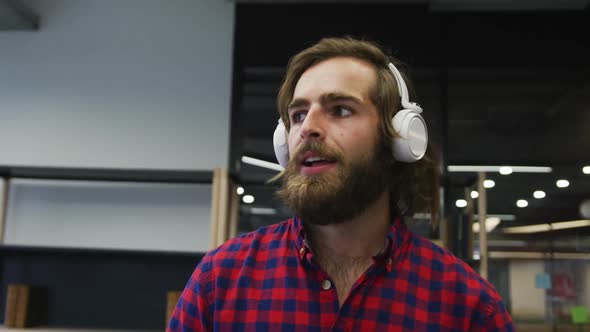 Caucasian businessman walking wearing headphones dancing in a modern office alt
