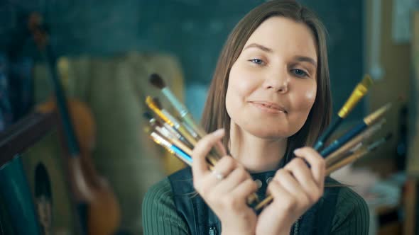 Young Smiling Women Painter with Many Brushes Looking at the Camera alt