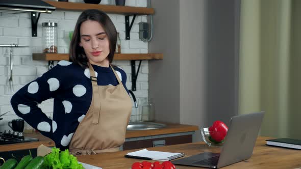 Tired woman writes culinary recipe in notebook massages neck after using laptop alt