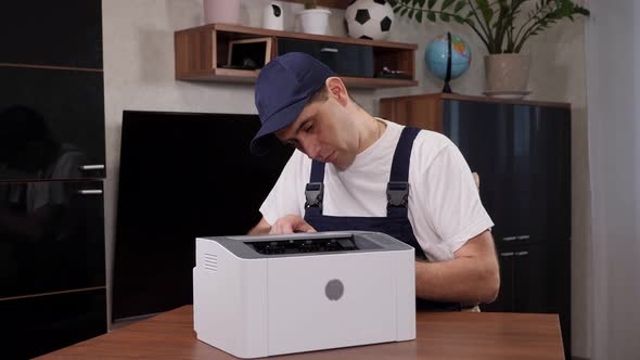 A Male Handyman in a Blue Jumpsuit Repairs a Printer with a Screwdriver alt