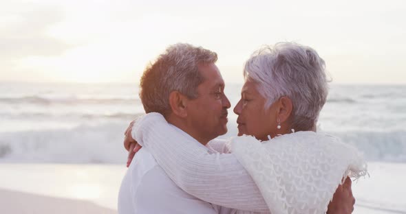 Happy hispanic just married senior couple kissing on beach at sunset alt