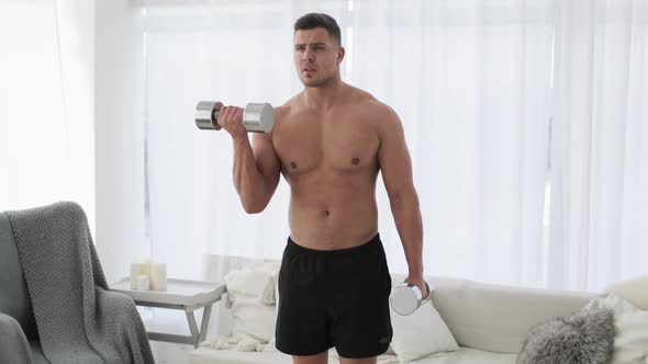 Man with Naked Torso Is Lifting Dumbbells at Home Practicing Biceps Exercise