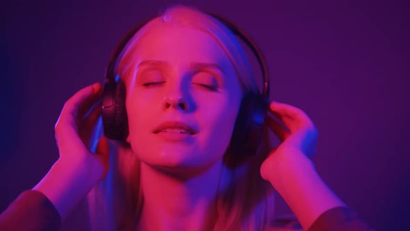 Attractive Woman Dances Vigorously to Rhythmic Music with Headphones Under Colored Lighting alt