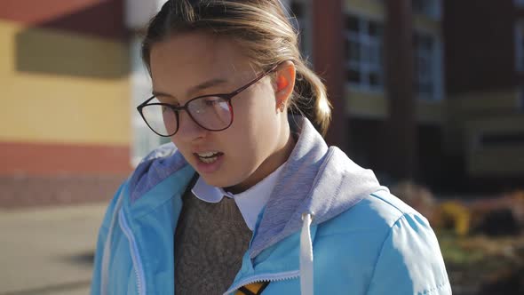 A Teenage Girl in a Blue Jacket and Glasses Reads a Synopsis Against the Background of an