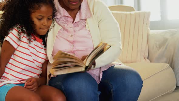Grandmother and daughter reading book in living room alt