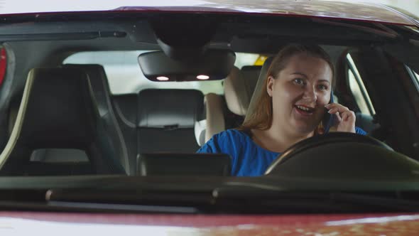 Young Stout Woman Talking on Smartphone and Smiling Sitting in Car Drive Seat alt
