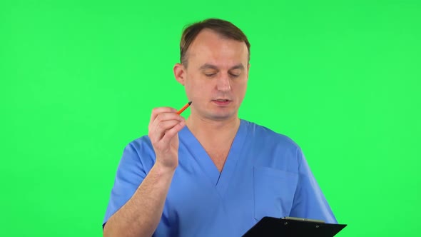 Medical Man Fills Papers at Black Folder with Pensil. Green Screen alt