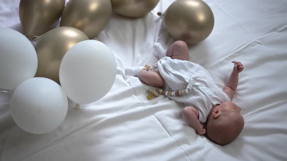 High Angle View Carefree Newborn Baby Lying on White Soft Comfortable Bed with Balloons Around alt