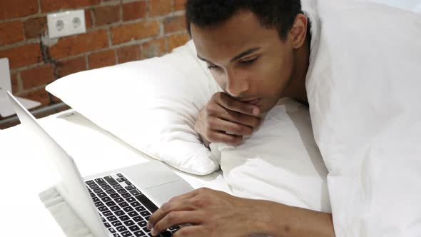Pensive African Man Lying in Bed Working and Thinking, Laptop alt