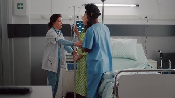 Medical Team Helping Patient to Stand Up From Bed Holding Intravenous IV Fluid Drip Bag alt