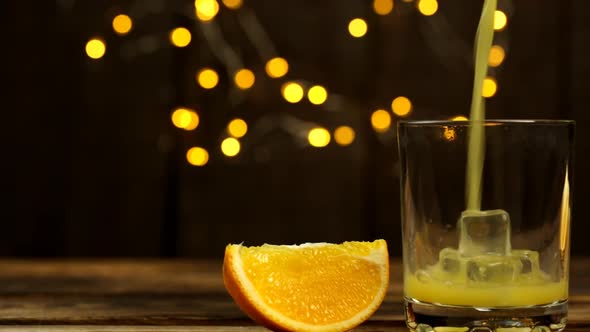 One Slice Of Orange And Juice Is Poured Into A Glass With Lights In The Background