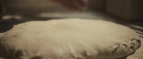 Chef spreading white flour over a fresh unprepared italian pizza dough. alt