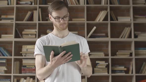Middle Shot of Confident Caucasian Man in Eyeglasses Turning Book Page and Smiling. Portrait of alt