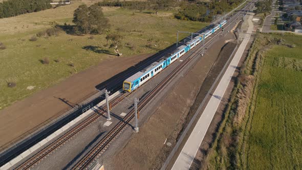 Train drives through outer suburbs aerial shot rising alt