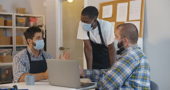 Small Business Owners in Safety Mask Discuss Strategy on Laptop in Warehouse alt