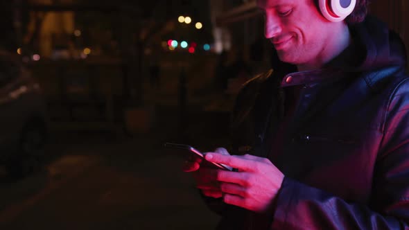 Caucasian hooded male wearing headphones, smiling, lying on the wall, in the evening alt