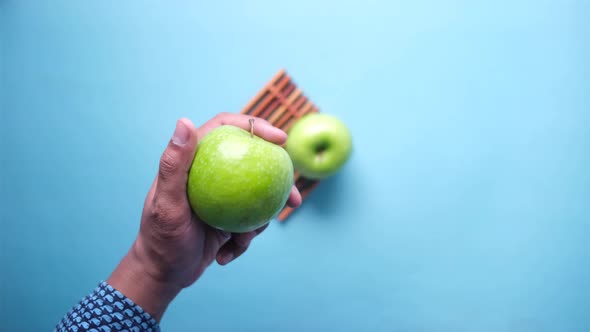 Hand Holding Green Apple on Blue Background