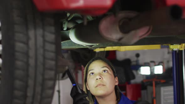 Female mechanic using a led lamp and working under a car at a car service station alt