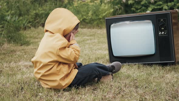 Small Child is Watching an Old Strobing TV and Covers His Eyes with His Palms alt