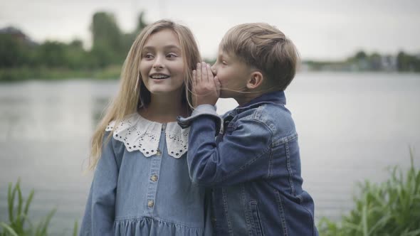 Portrait of Cute Caucasian Boy Whispering on Ear of Excited Pretty Girl alt