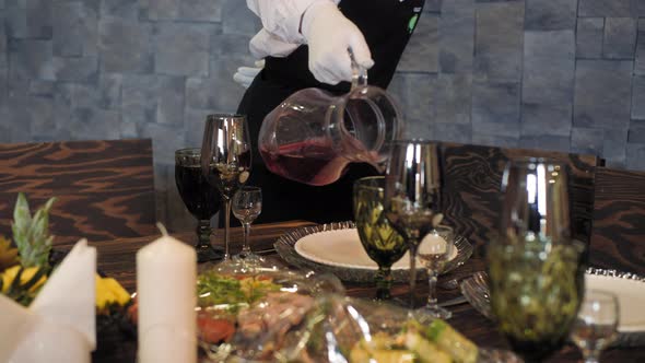 Waitress Pouring Drink in Goblets Arranged By Food Served on Table