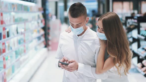 Girl in Mask Hugs Her Boyfriend While Viewing Reviews on Cosmetic Products alt