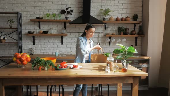 A Beautiful Young Woman in a Good Mood is Sorting Vegetables From a Bag and Putting Them on the alt