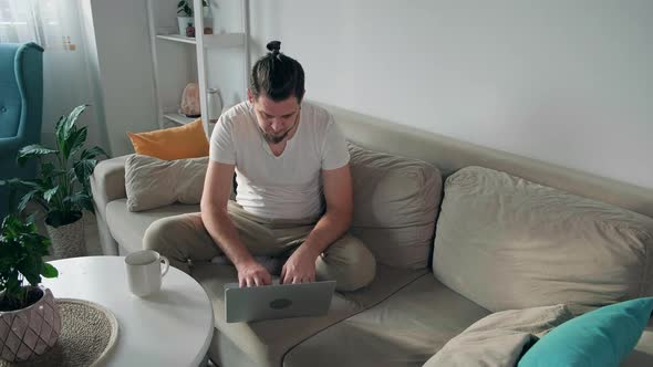 Young Man Using Laptop Typing and Working Sitting on the Couch at Home