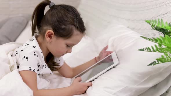 Cute Little Child Girl Lies in Bed Uses Digital Tablet